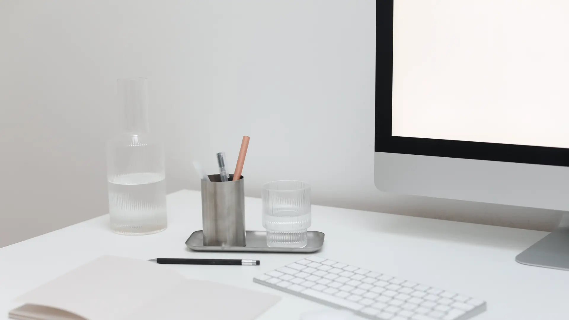 A monitor, keyboard and notebook on a clean desk