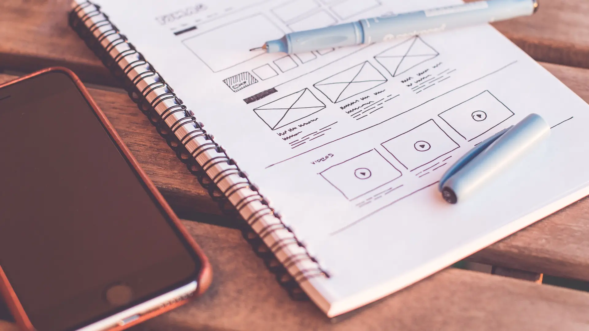 Hand-drawn website wireframes in a notebook, with a pen